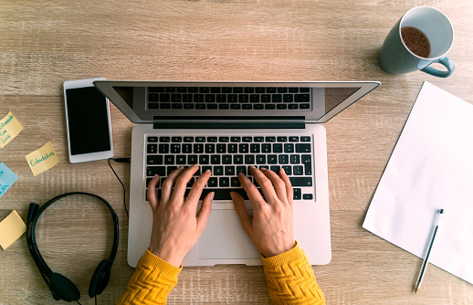 Close-up on a woman working online at home on her laptop and typing on the keyboard - telework concepts