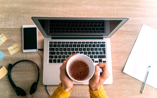 Close-up on a woman drinking coffee while working on her laptop at home - telework concepts