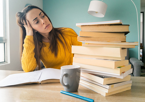 Frustrated female student looking at all the books she has to read while homeschooling - stay at home concepts