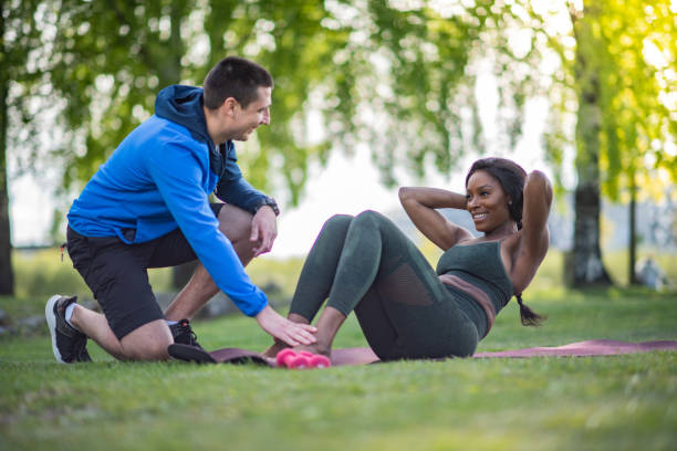 Sportswoman making sit-ups outdoors with the help of a trainer. stock photo