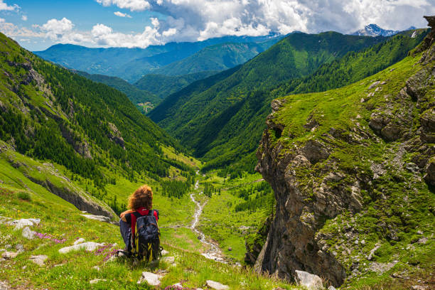 istock Woman with backpack resting on mountain top, looking at view dramatic landscape valley summer activity fitness wellbeing freedom concept, rear view 1254183530