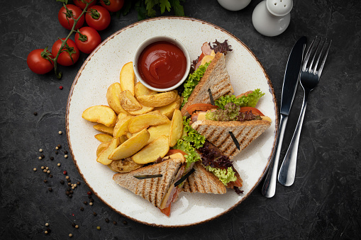 American club sandwich with french fries on a dark background