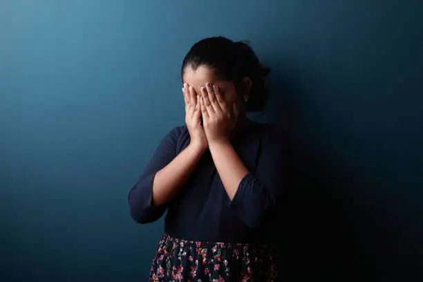 Photo of A girl feeling shame covering her face with hands.One light studio shot with shadow