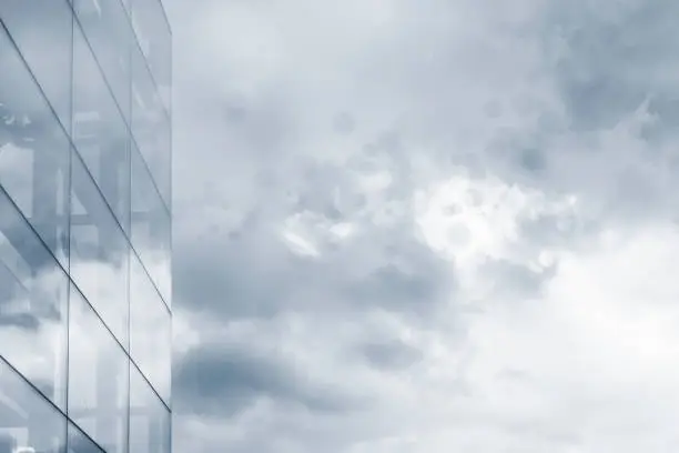 Glass wall fragment of modern building against cloudy sky. Light blue toned image. Business background with copy space for text.