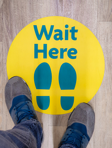 Personal perspective of a simple 'Wait Here' position sign on the floor of a supermarket to help with social distancing measures during the Covid-19 outbreak.
