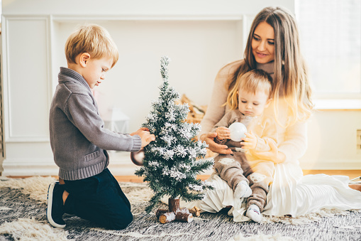Young mother with two son decorate the Christmas tree. Portrait loving family.