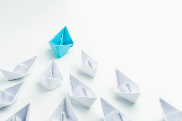 istock Leadership concept with blue paper ship leading among white on white background. 1254195999