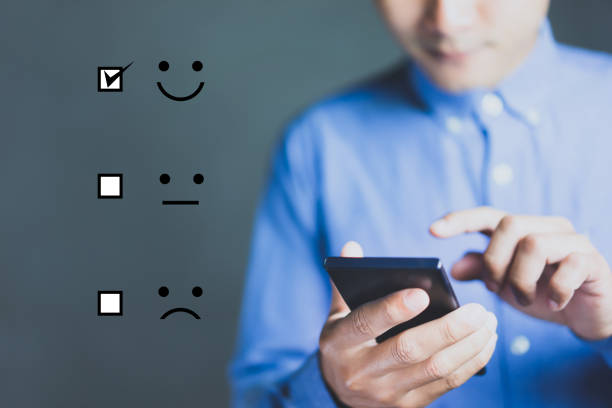 Businessman holding digital smartphone with a checked box on Excellent Smiley Face Rating for a Satisfaction Survey, Customer Experience Concept. stock photo