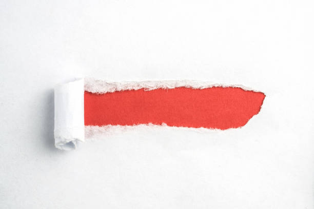istock Hole in white paper with torn sides over red paper background with space for text. Torn paper for web advertising and print. 1254196187