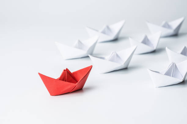 Leadership concept with red paper ship leading among white on white background. stock photo