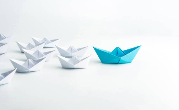 istock Leadership concept with blue paper ship leading among white on white background. 1254196421