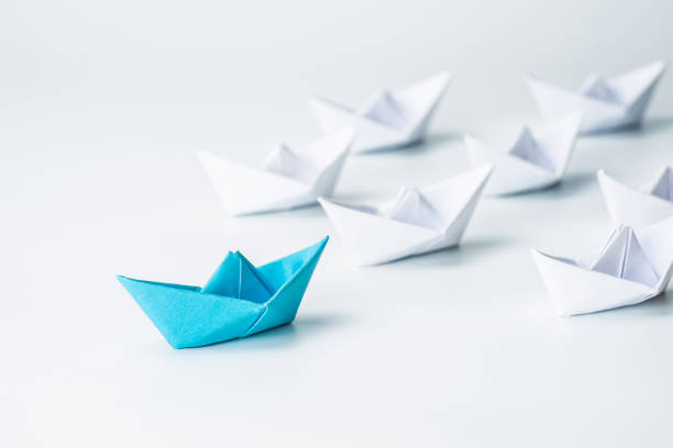istock Leadership concept with blue paper ship leading among white on white background. 1254197391