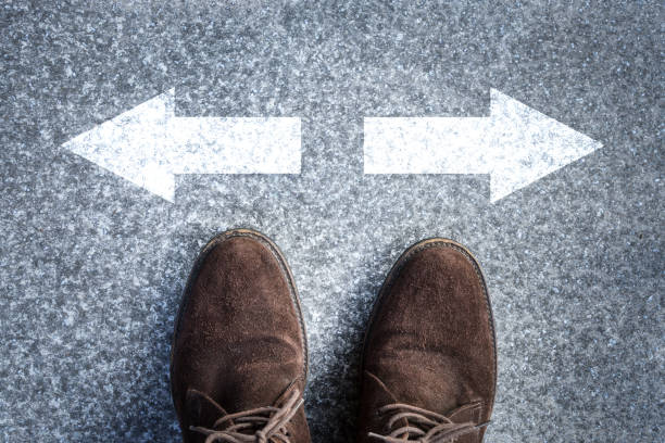 istock Man feet walking on asphalt road with arrow choice concept. 1254197471