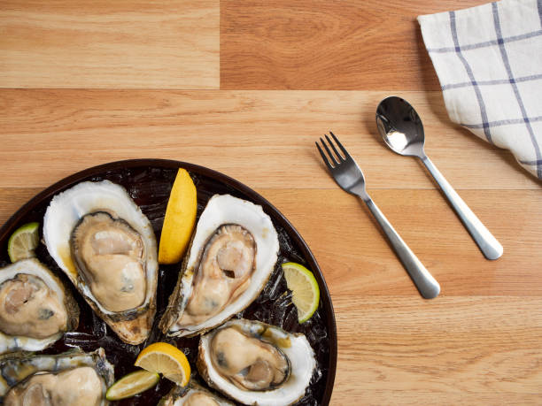 木製のテーブルの上のトレイに氷とレモンの新鮮なカキのクローズアップ。 - prepared oysters prepared shellfish shucked seafood ストックフォトと画像
