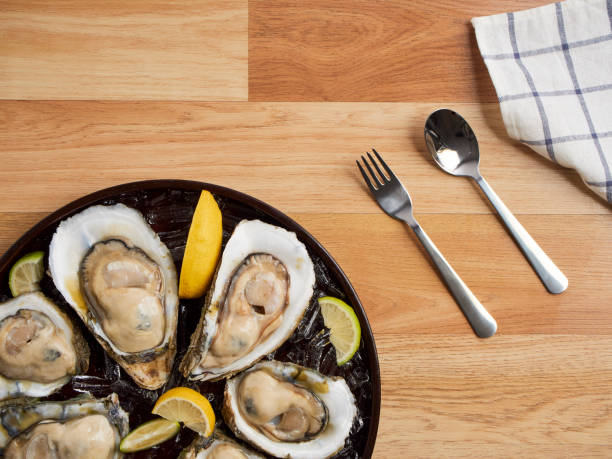 close-up de ostras frescas no gelo e limão na bandeja na mesa de madeira. - prepared oysters prepared shellfish shucked seafood - fotografias e filmes do acervo