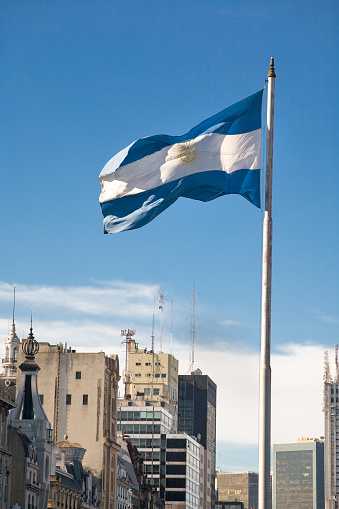 Argentinian flag waving against blue sky on a sunny day with city background