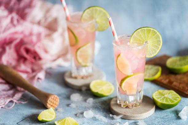 Fresh pink cocktails or mocktails with lime and grapefruit juice and crushed ice A fresh cocktail drink with lime and pink grapefruit juice. Paloma cocktail. Two glasses on the table and they have environmentally friendly paper straws. Blue gray background with copy space. tequila drink stock pictures, royalty-free photos & images