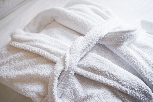 The concept of rest in a hotel. White Bathrobe on bed in bedroom close-up.