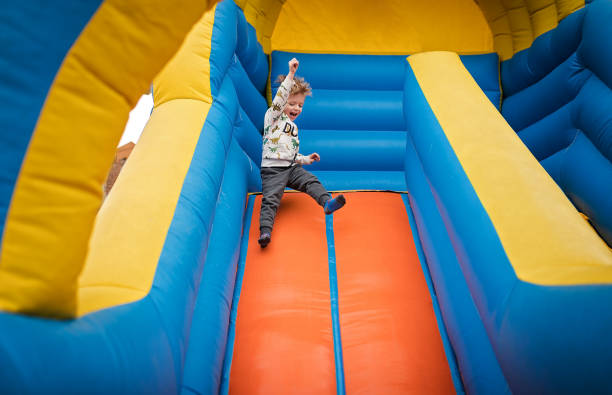 niño feliz deslizándose hacia abajo en un castillo hinchable - inflatable child playground leisure games fotografías e imágenes de stock