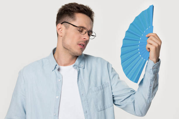 istock Overheated millennial man in eyeglasses waving fan. 1254205879