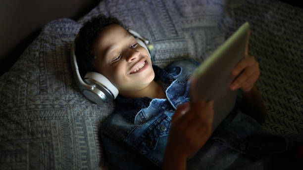 niño viendo una película usando una tableta digital en la cama - watching tv fotografías e imágenes de stock