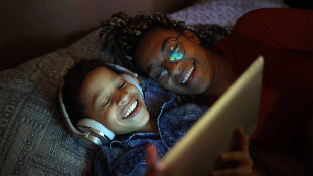 hermanos escuchando música usando una tableta digital en la cama - lying down women laptop freedom fotografías e imágenes de stock