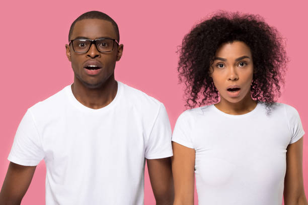 Amazed surprised young African American couple with open mouth Amazed surprised young African American couple with open mouth looking at camera, handsome young man in glasses and woman receiving unexpected news information, isolated on pink studio background unusual couple stock pictures, royalty-free photos & images
