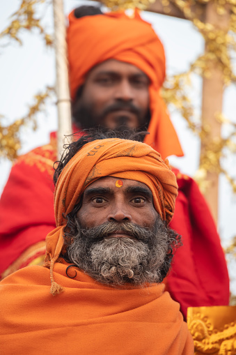 Two holy man posing in a parade float during the Royal Bath Procession. Photo taken during Kumbh Mela 2019 in Prayagraj (Allahabad), India. \nKumbh Mela or Kumbha Mela is a major pilgrimage and festival in Hinduism, and probably the greatest religious festival in the World. It is celebrated in a cycle of approximately 12 years at four river-bank pilgrimage sites: the Allahabad (Ganges-Yamuna Sarasvati rivers confluence), Haridwar (Ganges), Nashik (Godavari), and Ujjain (Shipra). The festival is marked by a ritual dip in the waters, but it is also a celebration of community commerce with numerous fairs, education, religious discourses by saints, mass feedings of monks or the poor, and entertainment spectacles. Pilgrims believe that bathing in these rivers is a means to cleanse them of their sins and favour a better next incarnation.