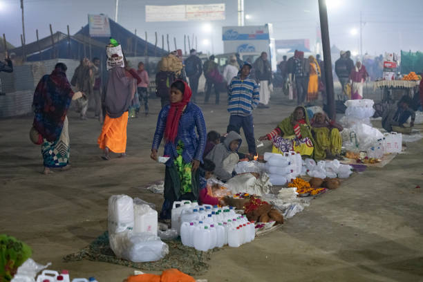 Street hawkers in Kumbh Meka Women selling various kinds of water containers, to be filled with holy water during the holy dip. Photo taken at night, on a Royal Bath's eve, during Kumbh Mela 2019 in Prayagraj (Allahabad), India. 
Kumbh Mela or Kumbha Mela is a major pilgrimage and festival in Hinduism, and probably the greatest religious festival in the World. It is celebrated in a cycle of approximately 12 years at four river-bank pilgrimage sites: the Allahabad (Ganges-Yamuna Sarasvati rivers confluence), Haridwar (Ganges), Nashik (Godavari), and Ujjain (Shipra). The festival is marked by a ritual dip in the waters, but it is also a celebration of community commerce with numerous fairs, education, religious discourses by saints, mass feedings of monks or the poor, and entertainment spectacles. Pilgrims believe that bathing in these rivers is a means to cleanse them of their sins and favour a better next incarnation. prayagraj photos stock pictures, royalty-free photos & images
