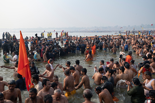 Overview of the confluence of the Ganges and Yamuna rivers, during the Royal Bath morning. Some holy man, or religious leaders pose on the centre, surrounded by lay men, while a crowd of photographers take their shots. It is believed that taking the holy dip ath the same time as the holy man, increases its power. Photo taken during Kumbh Mela 2019 in Prayagraj (Allahabad), India. \nKumbh Mela or Kumbha Mela is a major pilgrimage and festival in Hinduism, and probably the greatest religious festival in the World. It is celebrated in a cycle of approximately 12 years at four river-bank pilgrimage sites: the Allahabad (Ganges-Yamuna Sarasvati rivers confluence), Haridwar (Ganges), Nashik (Godavari), and Ujjain (Shipra). The festival is marked by a ritual dip in the waters, but it is also a celebration of community commerce with numerous fairs, education, religious discourses by saints, mass feedings of monks or the poor, and entertainment spectacles. Pilgrims believe that bathing in these rivers is a means to cleanse them of their sins and favour a better next incarnation.