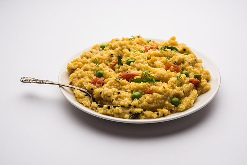 Vegetable Dalia or Daliya Khichadi or Broken Wheat Khichdi with tomato, green peas and chilli, served in a bowl or plate