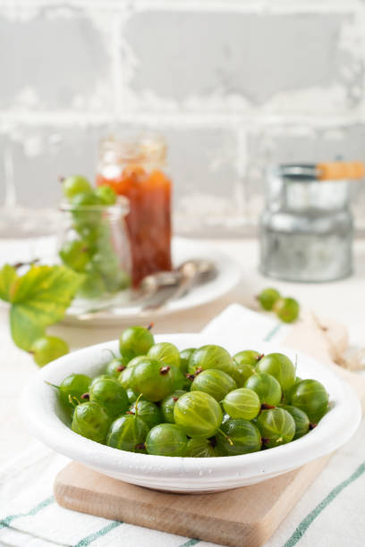 istock Fresh raw gooseberry berries in  white ceramic plate on light wooden background. Selective focus. Rustic style. 1254234308