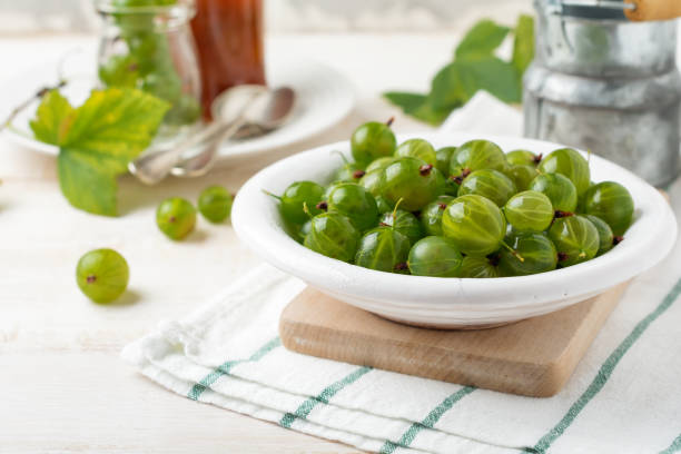 istock Fresh raw gooseberry berries in  white ceramic plate on light wooden background. Selective focus. Rustic style. 1254234419