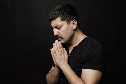 Praying man portrait over black background