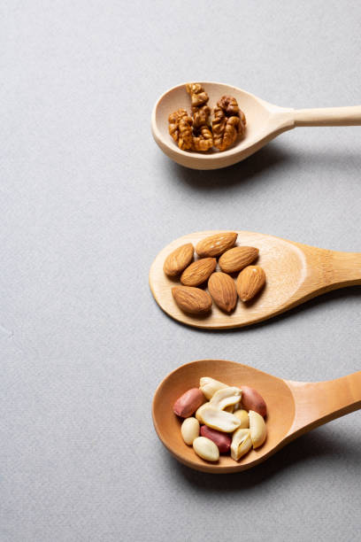 istock Dried hazelnut, cashew, almonds in wood spoons on grey. Vertical. Minimalism concept 1254241532