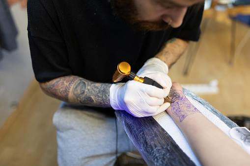 Tattoo artist making a tattoo on young woman’s wrist indoor, horizontal, tattoo studio