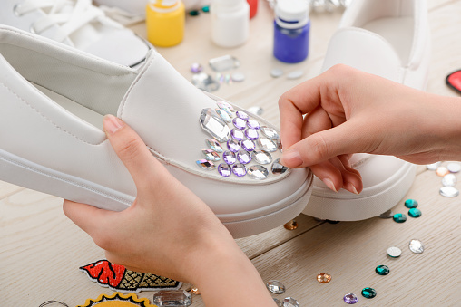 Girl putting rhinestones onto shoes. Creative concept and artistic touch to boring footwear. Custom design and fashion.