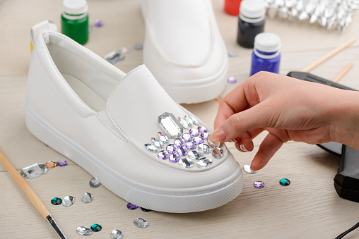 Girl adding rhinestones to white slip-on shoes. Fashion and DIY projects. Giving footwear a fabulous sparkling look.