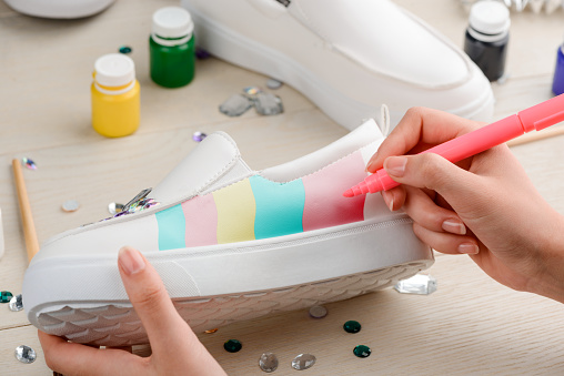 Girl painting white slip-on shoes with felt-tip pen, composition of colorful stripes. Fashion and handmade design.