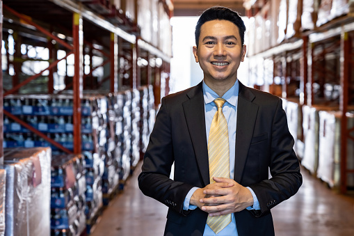 Portrait of asian confidence businessman investor stand in large factory and distribution warehouse environment. Business owner and investment concept.