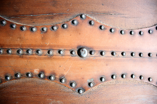 close up shot of leather hinges, straps, and metal rivets from brown antique steamer trunk