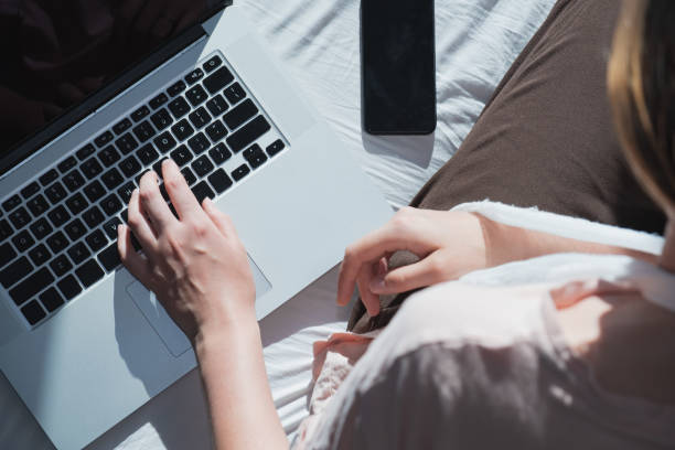 istock Woman with wounded arm sits in bed next to a computer and phone. 1254257231