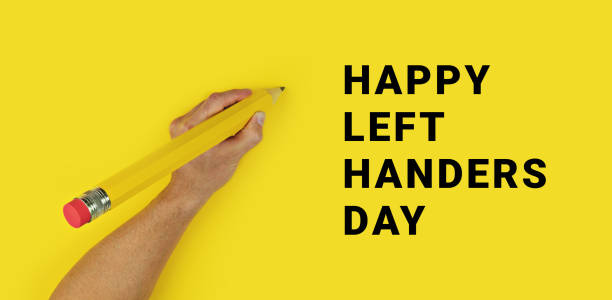 grande matita nella mano sinistra maschile su sfondo giallo con testo happy left handers day. striscione concettuale per la celebrazione della giornata internazionale del mancino - left handed foto e immagini stock
