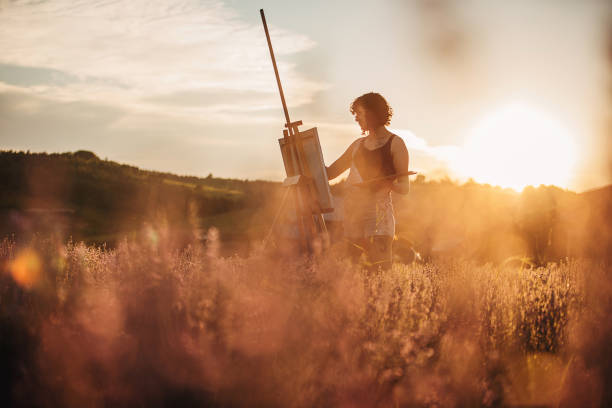 One woman, beautiful female painter artist painting on lavender field outdoors on a sunny day.