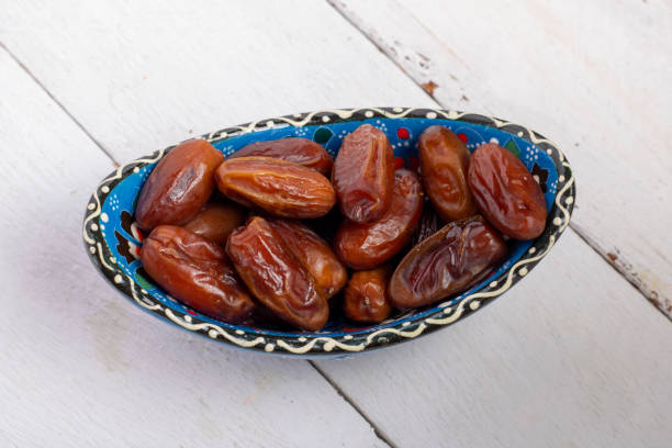 istock Dates fruit in a blue bowl closeup on white wooden background 1254271460