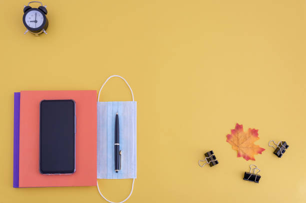 workbooks, pen, watch, smartphone, face mask on yellow background