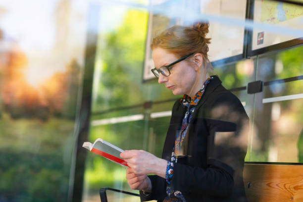 istock Woman reading a book at a bus stop 1254272911