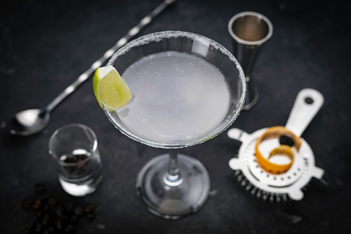 A glass of blue lagoon cocktail with a cherry, a slice and peel of an orange and ice stands on a gray background. Close-up.