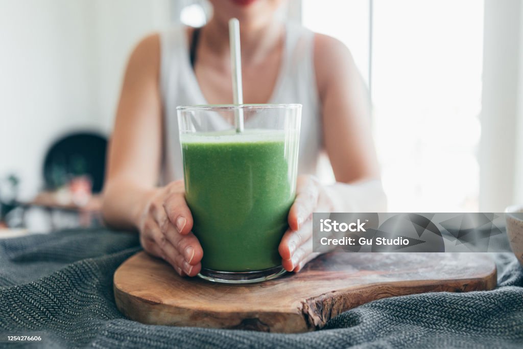 A Balanced Vegan Diet & Sustainable Lifestyle Cropped and close-up shot of young woman holding and drinking a glass of green smoothie for breakfast. Smoothie Stock Photo