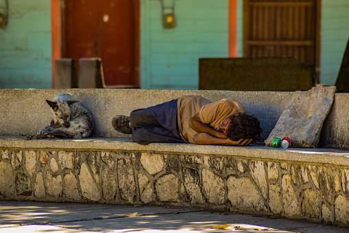 A Cuban man and his dog sleep on a concrete seating area in a town square in Cuba